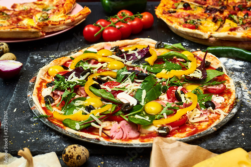 Raw pizza with mozzarella cheese, meat, tomatoes, mushrooms, peppers, herbs on a dark wooden background. Cooking delicious italian pizza.