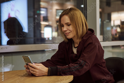 A woman is sitting at a table in a public place with a telephone.