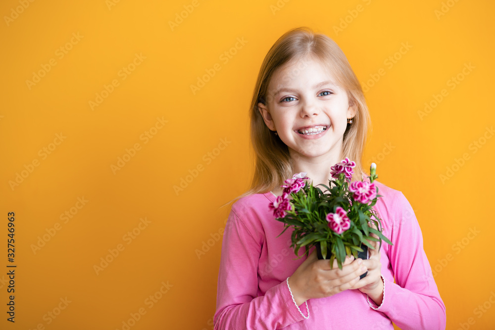 Cute baby on an orange background, 6-8 years old, a girl in pink clothes smiles, holds a pot with a flower of cloves in her hands Cute baby on an orange background, 6-8 years old, a girl in pink clothes smiles, holds a pot with a flower of cloves in her hands