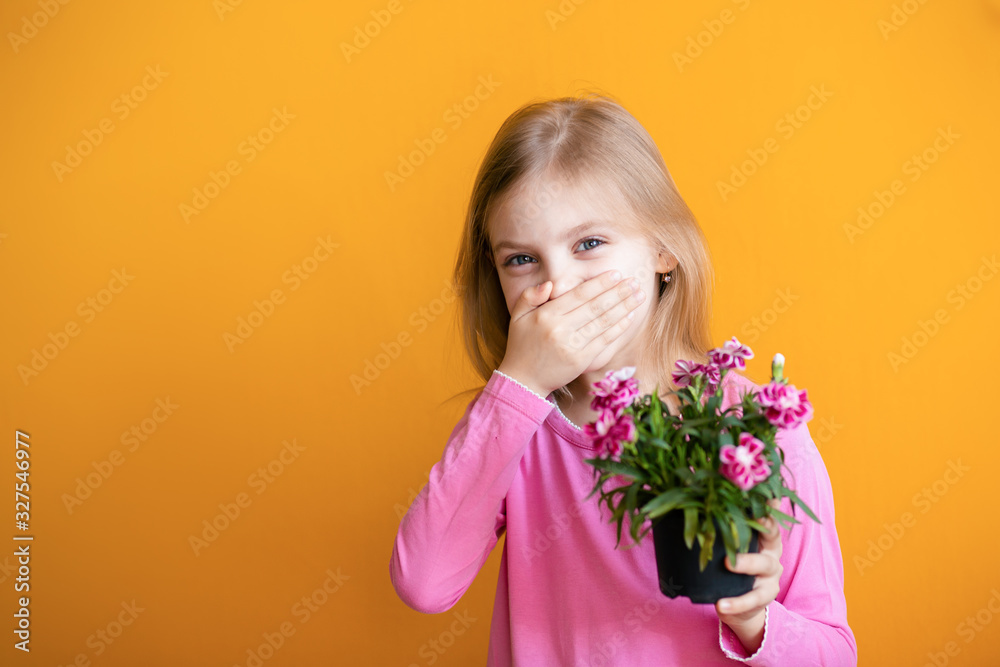 cute baby on an orange background, 6-8 years old, a girl in pink clothes sneezes from allergies, holds a pot with a flower of cloves in her hands cute baby on an orange background, 6-8 years old, a girl in pink clothes sneezes from allergies, holds a pot with a flower of cloves in her hands