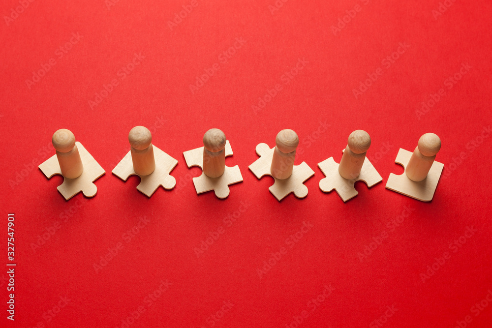 Obraz premium Wooden figures on puzzles on red background as a symbol of team building. Organization group people in business. Cooperation and partnership.