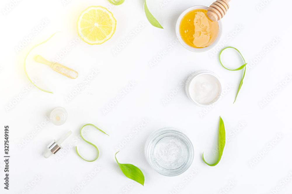 Fototapeta Natural organic ingredients to make home skin care. Cleansing and nourishing cosmetics. Beauty products: cream, honey, sea salt among green leaves on white background. Flat lay, copy space for text