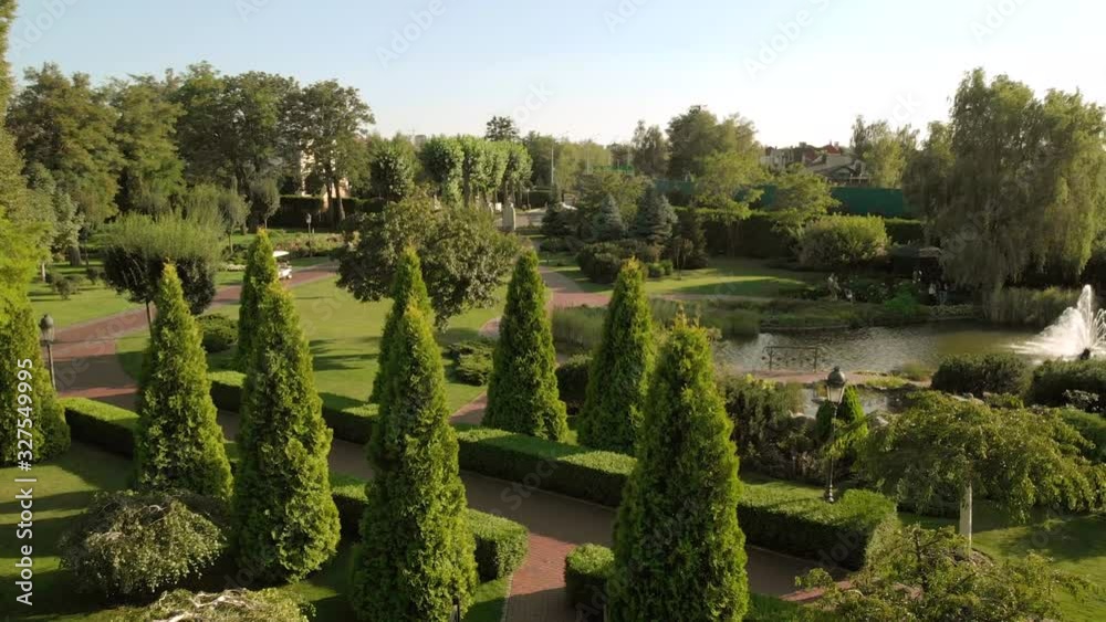 Flying above well-groomed garden park. Artificial pond with fountain. Walking people in a sunny park. Flying above well-groomed garden park. Artificial pond with fountain. Walking people in a sunny park.