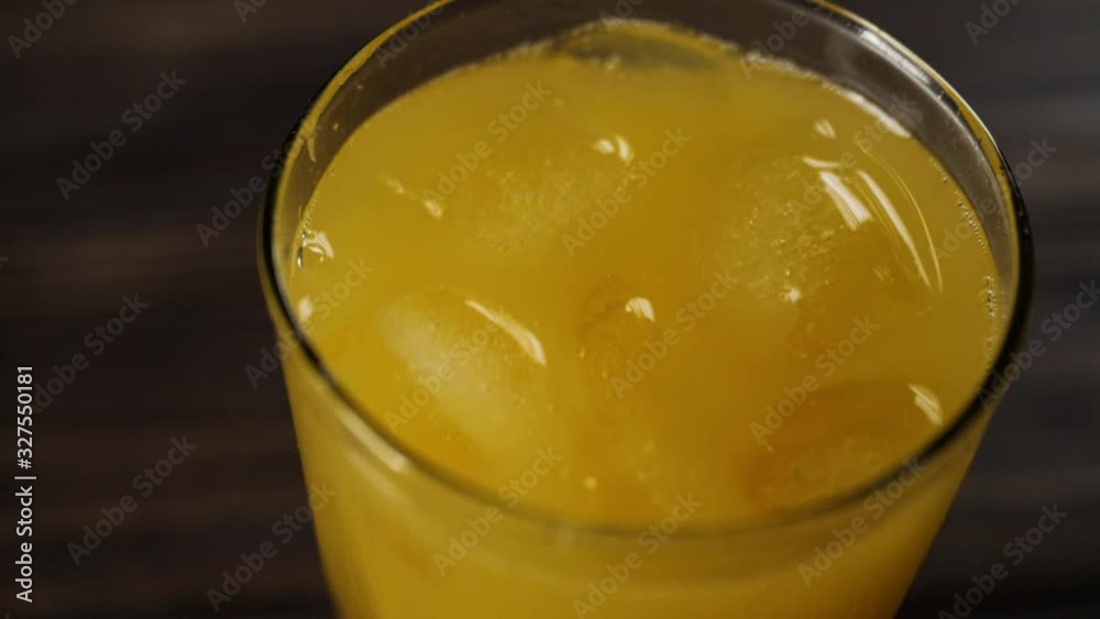 Top view of ice cubes spin and float in fresh orange juice in a tall glass on wooden table Top view of ice cubes spin and float in fresh orange juice in a tall glass on wooden table