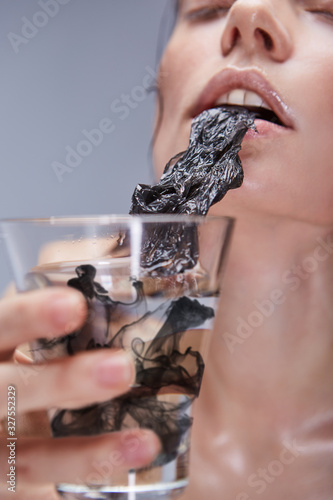 The environmental pollution is destroying human health and our planet. A thirsty lady is trying to suck a black polythene substance from the glass with dirty water. 