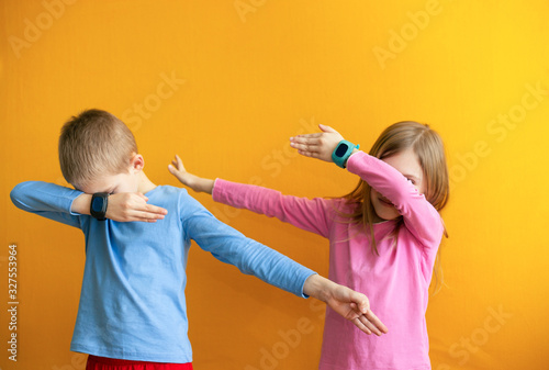 Children 6-8 years old on an orange background with a smart GPS watch make a cool young gesture 