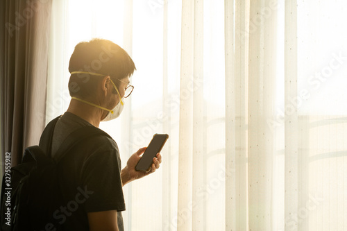 Traveller wearing surgical mask to prevent flu disease Coronavirus using smartphone and standing at the window at sunset photo