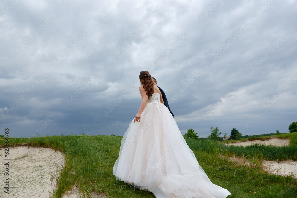 Full length body portrait of young bride and groom walking on green grass of golf course, back view. Happy wedding couple, copy space
