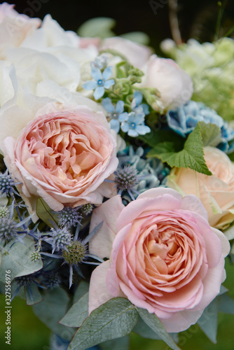 Close up of bridal bouquet of pink roses  blue flowers and greenery on white wood chair outdoors  copy space. Wedding concept