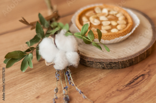 A peanut cake on a natural wood stand on a rumbled wooden background. Decor of cotton and lavender flowers. Candy store, coffee shop. Soft focus