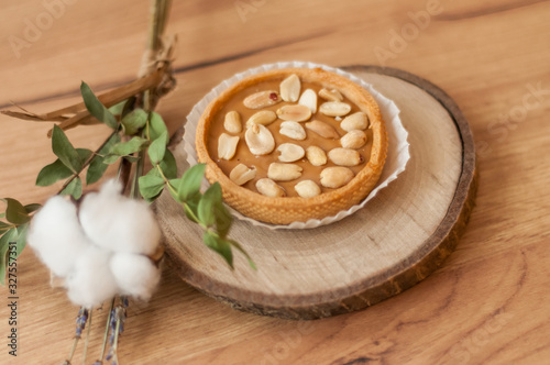 A peanut cake on a natural wood stand on a rumbled wooden background. Decor of cotton and lavender flowers. Candy store, coffee shop. Soft focus