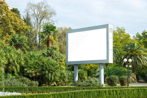 Blank street billboard poster in the park on the background of tropical plants. information banner, copy space for text.