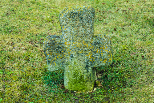 The alone ancient christian tomb cross  with runes covered with moss and lichen among green grass on the cemetry