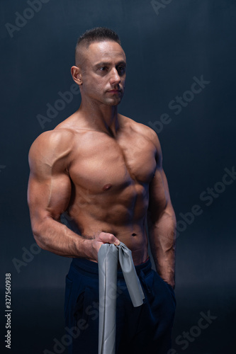 Obraz na płótnie Muscular man doing calisthenic exercise with power band isolated on the black ba