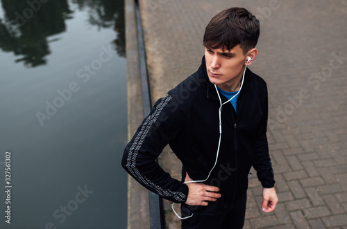 Image of young athlete man posing outdoor in the morning on the fog nature background during running. Fitness male exercising in the park and listenting the music on earphones. People, sport concept photo