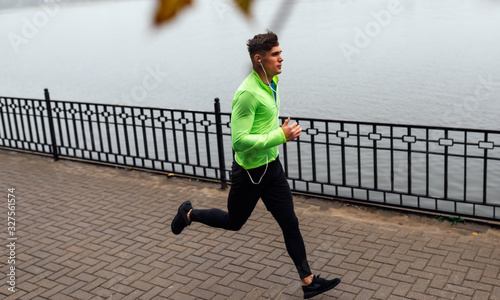 Athelte man running in the morning on the fog lake background. Runner male jogging in the park and listenting the music on earphones. People and sport concept photo
