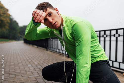 Horizontal image of athletic man stretching outdoor in the morning on the fog nature background. Fitness male exercising in the park and listenting the music on earphones. People and sport photo