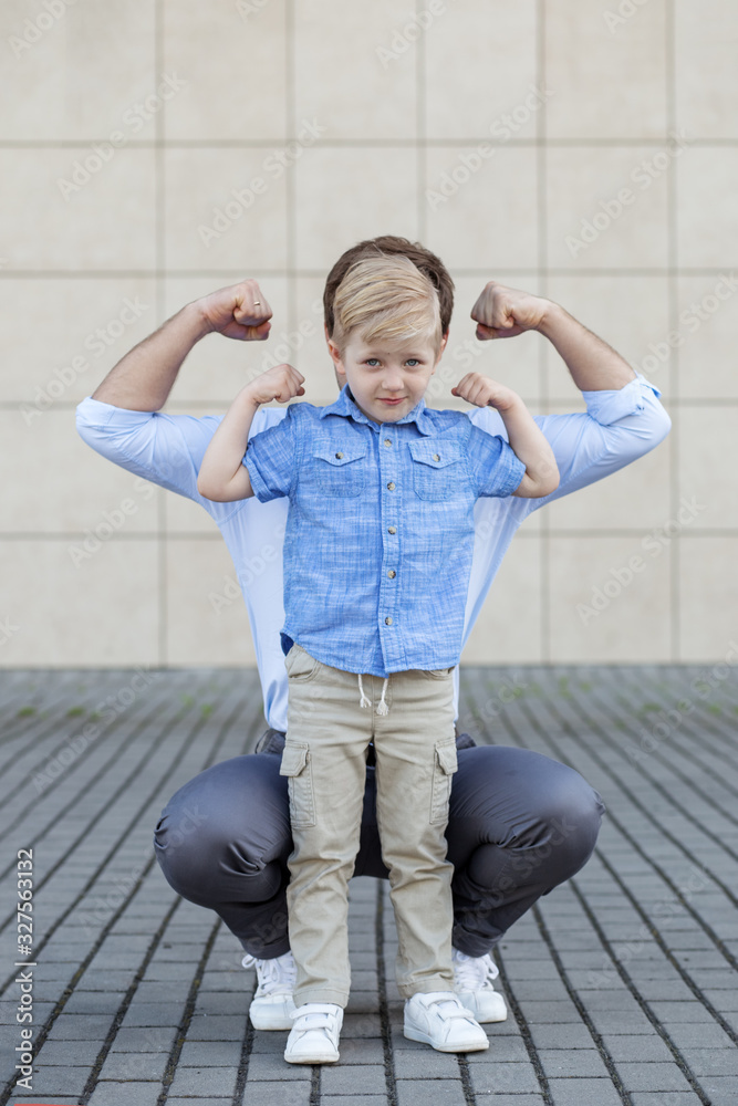 Dad and son are a preschooler playing. Show muscles. The concept of childhood, parenting and fatherhood Dad and son are a preschooler playing. Show muscles. The concept of childhood, parenting and fatherhood