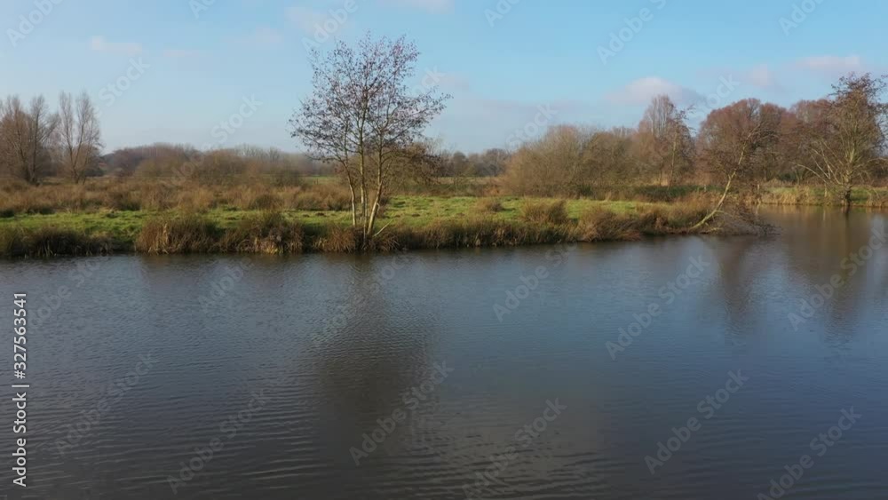 Flying over a large river following the riverbanks with small trees and broad fields with green grass on a sunny winter day in europe Flying over a large river following the riverbanks with small trees and broad fields with green grass on a sunny winter day in europe