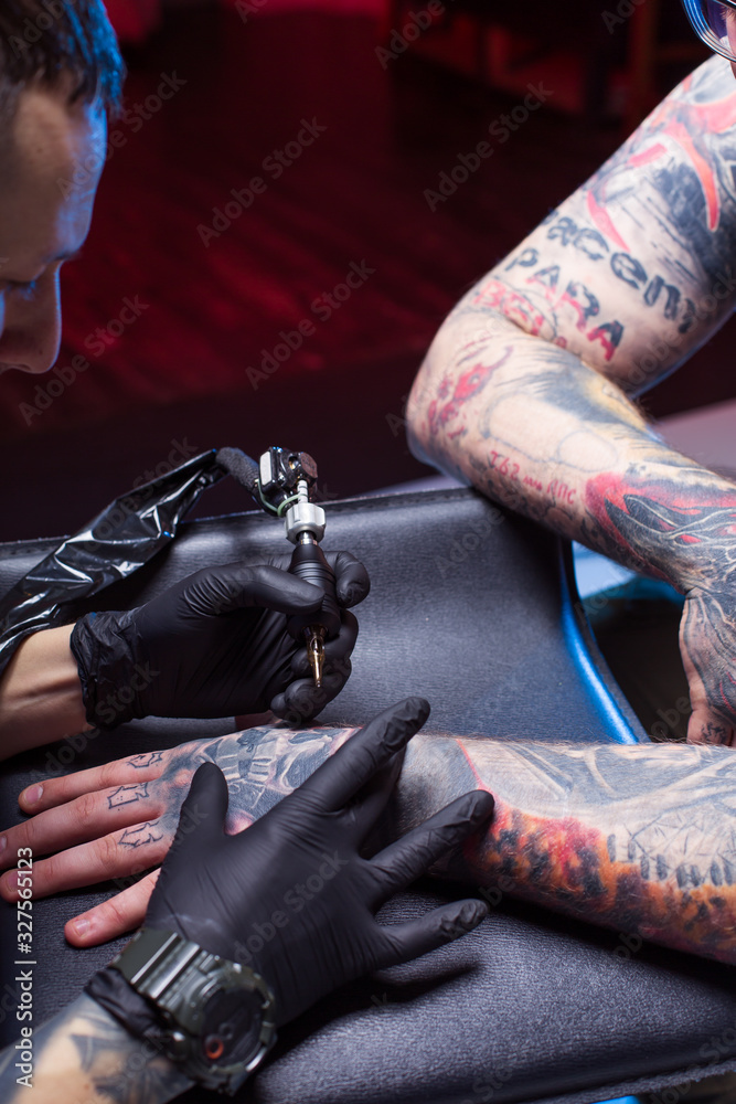 man artist tattoos in studio beats tattoos. Unusual male profession. An  informal punk rocker clogs a sleeve arm. Sterile gloved procedure. Ink  device tattoo machine. self-expression individuality Photos | Adobe Stock