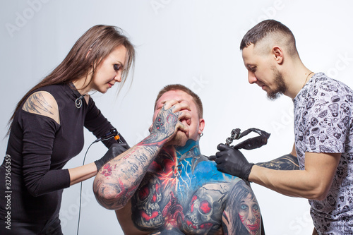 Tattooer artist beats a tattoo to a bearded man in sterile gloves. Tattoomachine. The process is painful. Pain from drawing with a needle. Informal punk rocker. stabbed the chest