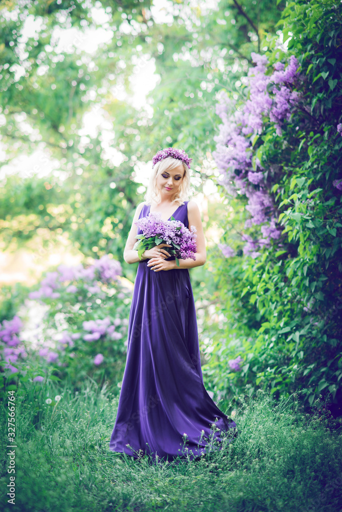Outdoor fashion photo of a beautiful young woman surrounded by purple flowers. Girls in a long dress with a slit on the background of a spring garden with lilacs. The concept of cosmetics and perfumes Outdoor fashion photo of a beautiful young woman surrounded by purple flowers. Girls in a long dress with a slit on the background of a spring garden with lilacs. The concept of cosmetics and perfumes