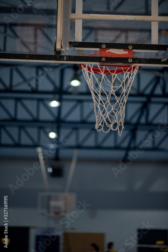 An interior space of a basketball court showing a scaffolding metal roof sheet with a framework of metal truss with sunlight goes through and a basketball ring as a focal point. © athichoke.pim