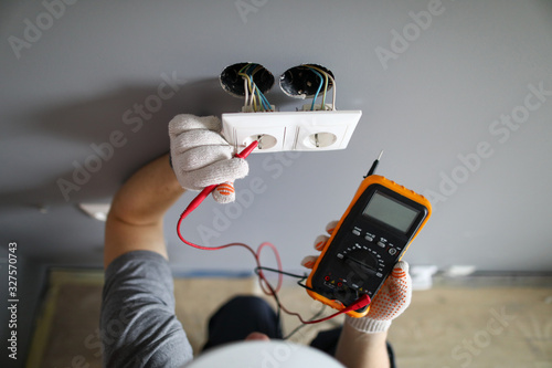 Man in hard hat and protective gloves checking wal outlet with tester photo
