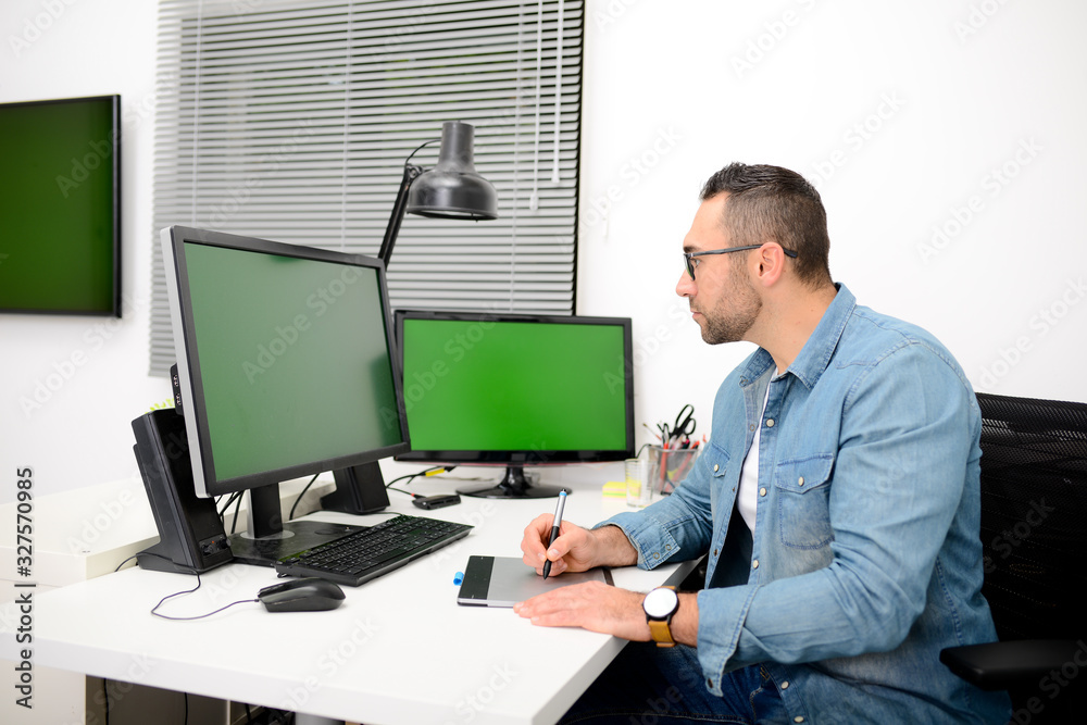 handsome young man graphic artist working in office desk with a computer and a graphic tablet