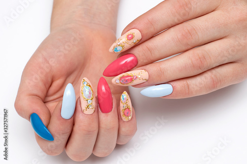 Exclusive manicure. Blue, dark blue, pink, beige, red manicure on long sharp nails. Stilettos. Falga, liquid stones, crystals, a brooch on the nails. Close up on a white background.