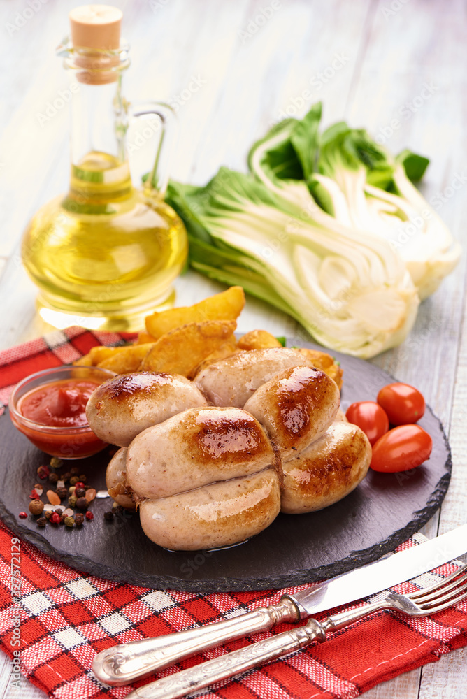 Grilled sausages, bratwurst with tomato sauce, spices and herbs on a stone plate, rustic background Grilled sausages, bratwurst with tomato sauce, spices and herbs on a stone plate, rustic background