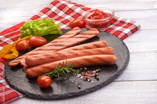 Grilled sausages with tomato sauce, spices and herbs on a stone plate, rustic background