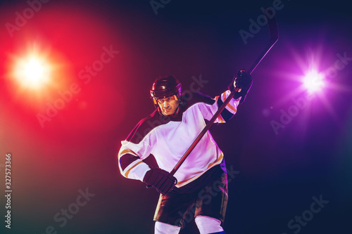 Winner. Male hockey player with the stick on ice court and dark neon colored background. Sportsman wearing equipment, helmet practicing. Concept of sport, healthy lifestyle, motion, wellness, action. © master1305