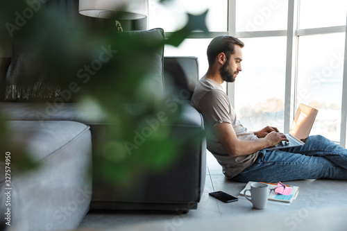 Concentrated young man using laptop computer sit on floor.
