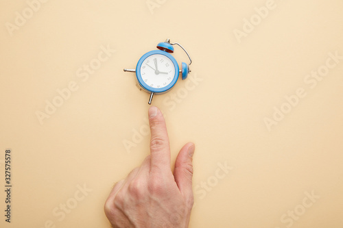Fototapeta Naklejka Na Ścianę i Meble -  cropped view of man touching small alarm clock on beige background