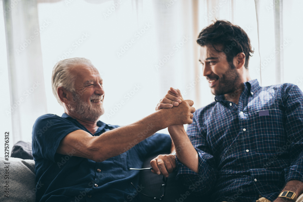 Sweet bonding. Cheerful elderly man sitting on the sofa next to his adult son, hugging him and posing together with him