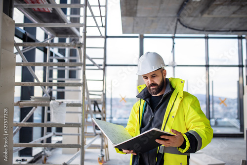 Man engineer standing on construction site, holding blueprints.