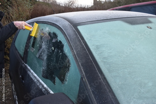 Frosty morning, ice cover window car, bad weather conditions, scraping ice from the car windows by hand with an ice scraper early in the morning