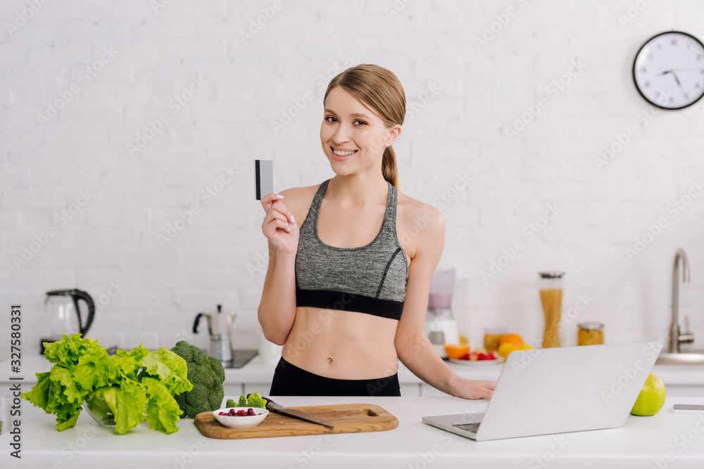Φωτογραφία happy girl holding credit card near laptop and food in kitchen
