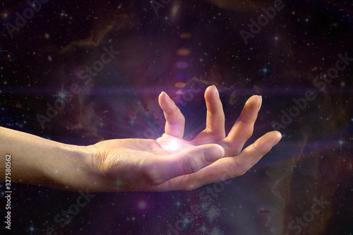 Female hand with light coming from the palm, against the background of the galaxy. The concept of divination, mysticism, predictions of the future.Elements of this image are provided by NASA.