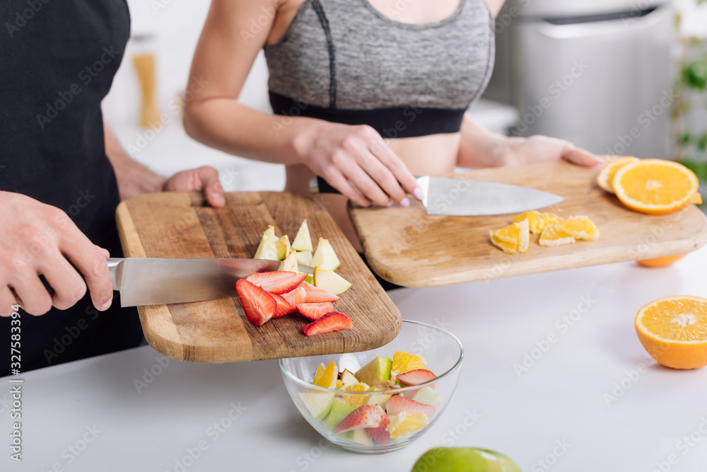 cropped view of man and woman cooking fruit salad
