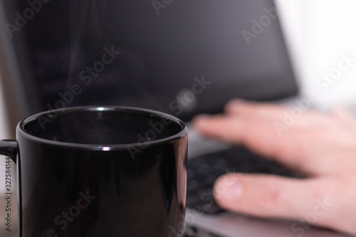 Black coffee mug with coffee with laptop, hand working in the background