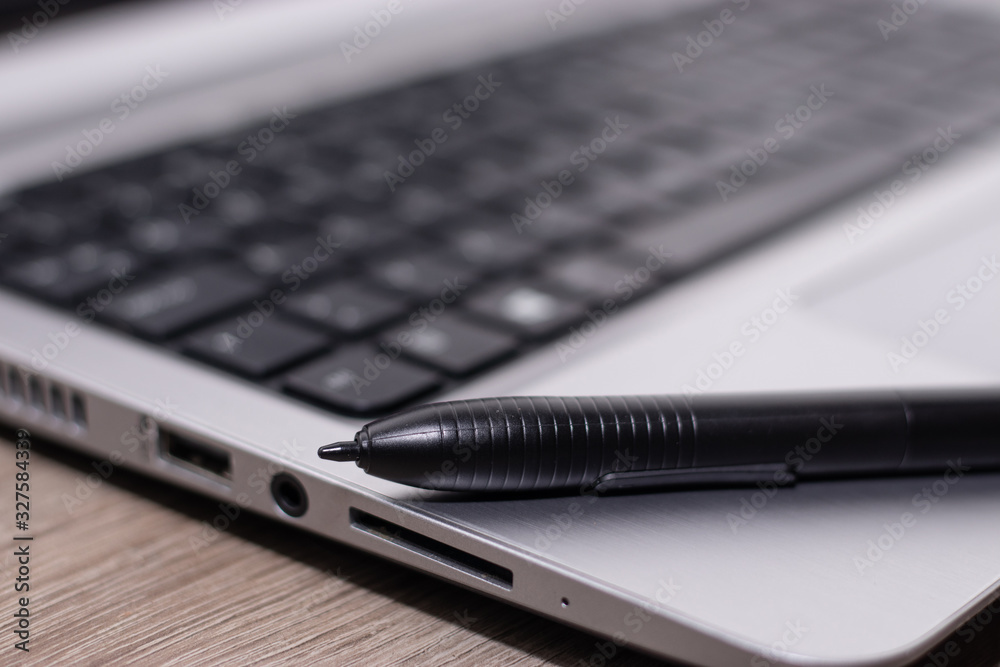 Black graphics tablet pen standing on a silver laptop Black graphics tablet pen standing on a silver laptop