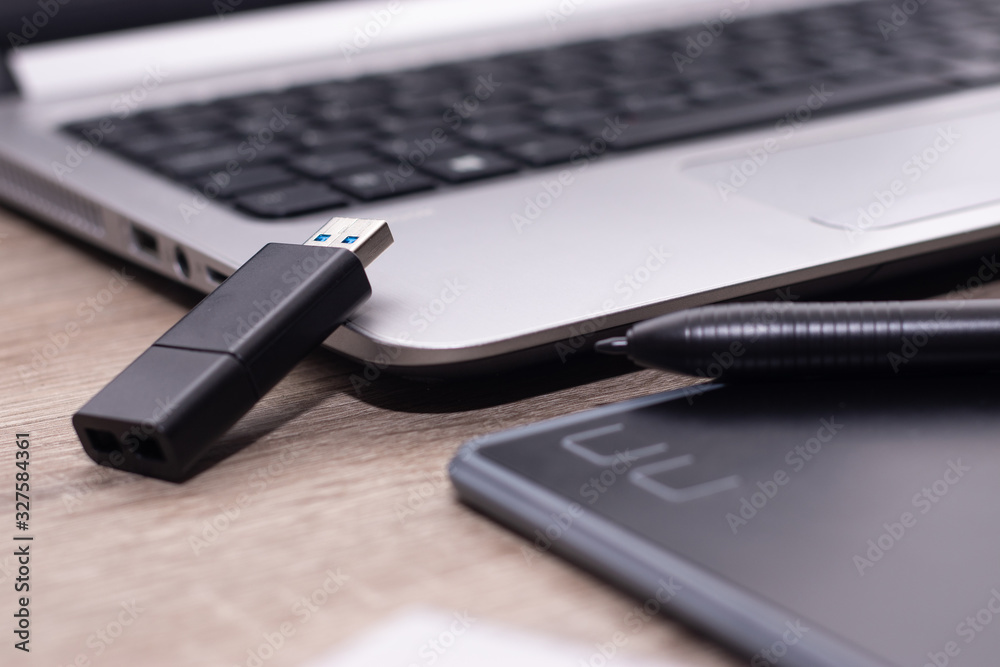 Black graphics tablet pen standing on a silver laptop, usb drive Black graphics tablet pen standing on a silver laptop, usb drive