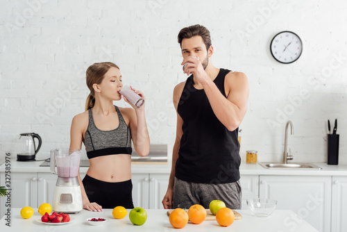 Quadro em tela sportive man and woman drinking tasty smoothie near fruits