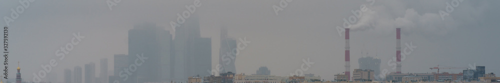 Industrial Moscow. Towers of Moscow City in evening fog. Chimneys with gray sky as background in winter. Industrial concept and ecology theme, heating season, modern global warming.