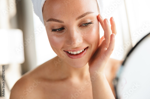 Photo of young joyful woman doing makeup while looking in mirror