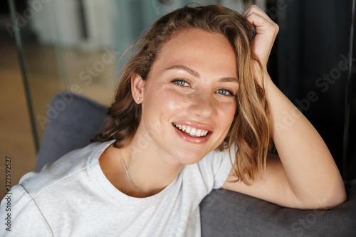 Image of happy caucasian woman smiling at camera while sitting on sofa photo