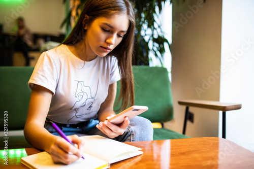 Young woman writes in her planner and holds mobile phone working freelance place