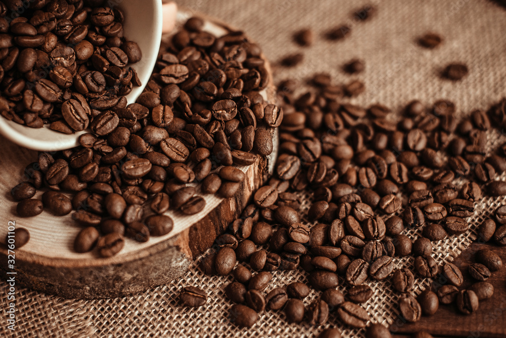 A Cup of coffee with scattered coffee beans on a burlap on a wooden background. Roasted natural coffee A Cup of coffee with scattered coffee beans on a burlap on a wooden background. Roasted natural coffee